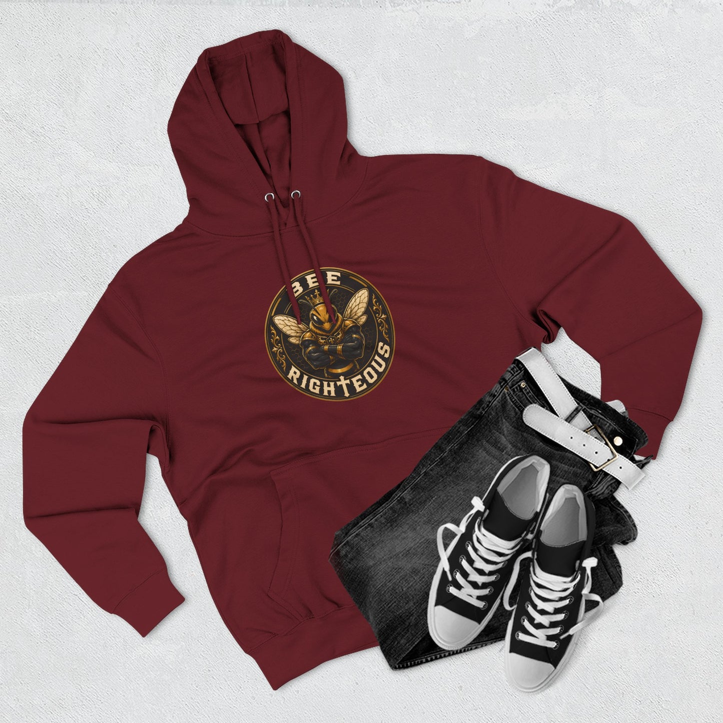 Maroon hoodie with a gold coin emblem, black jeans, and black sneakers on a light gray background