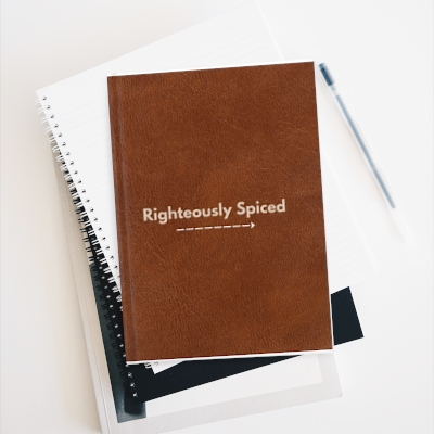 faux brown leather hard cover matte journal with the words "Righteously Spiced" in the middle and an arrow underneath pointing right. 