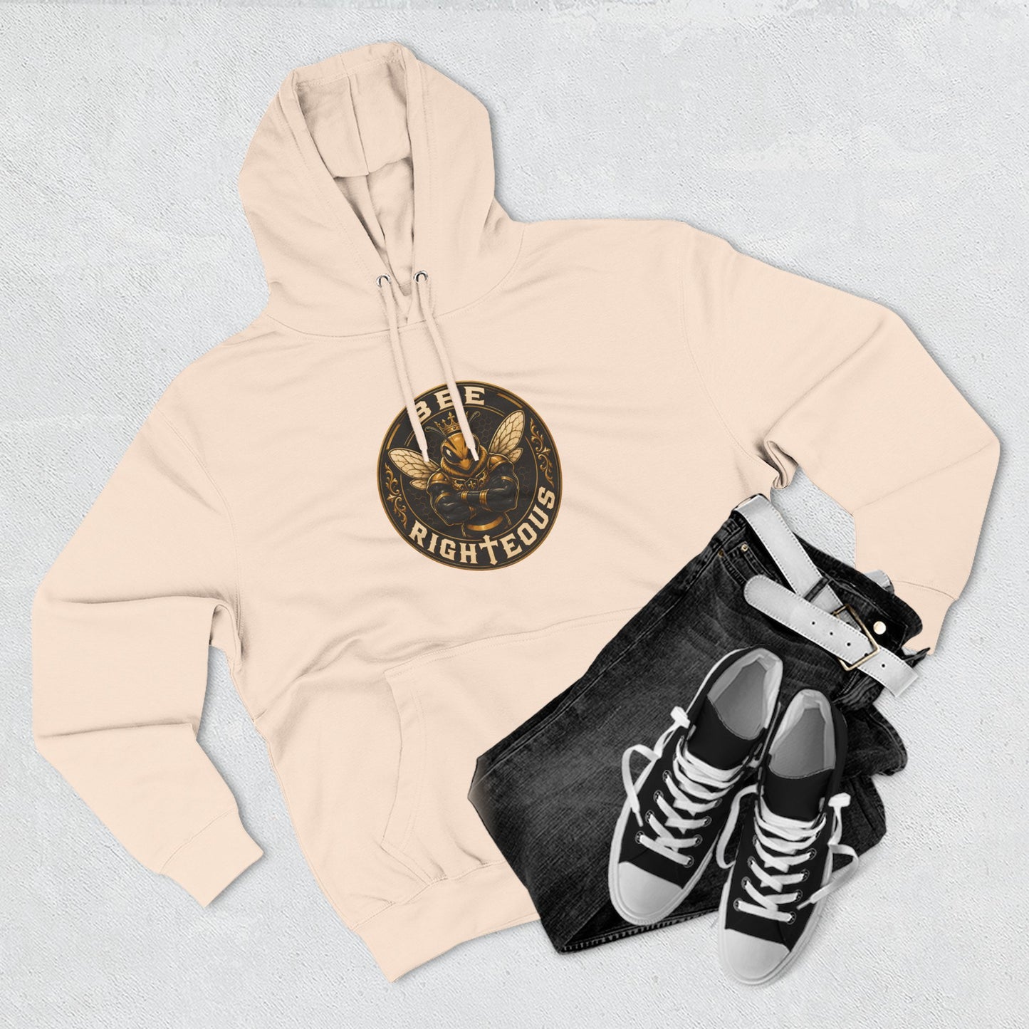 Beige hoodie with a logo, black jeans, and black sneakers on a light gray background